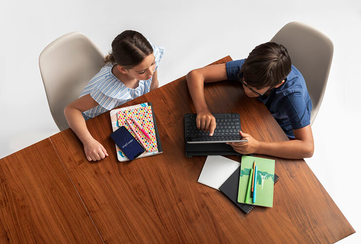 two kids sitting at table using devices