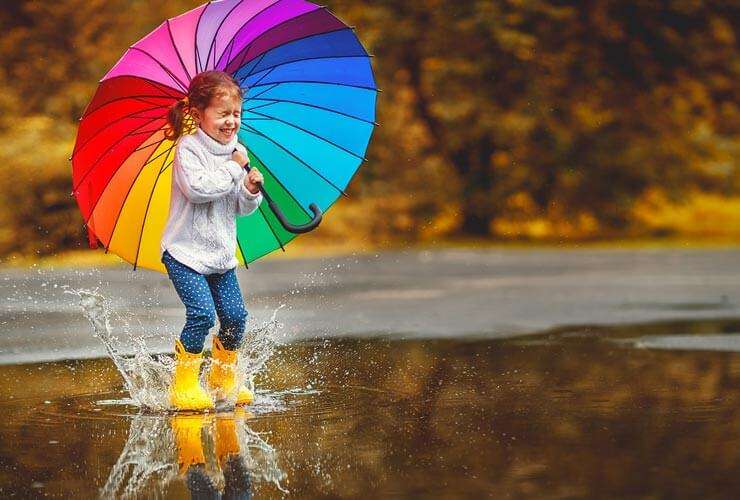 What to Watch this Spring - child with rainbow umbrella splashes in a spring rain shower