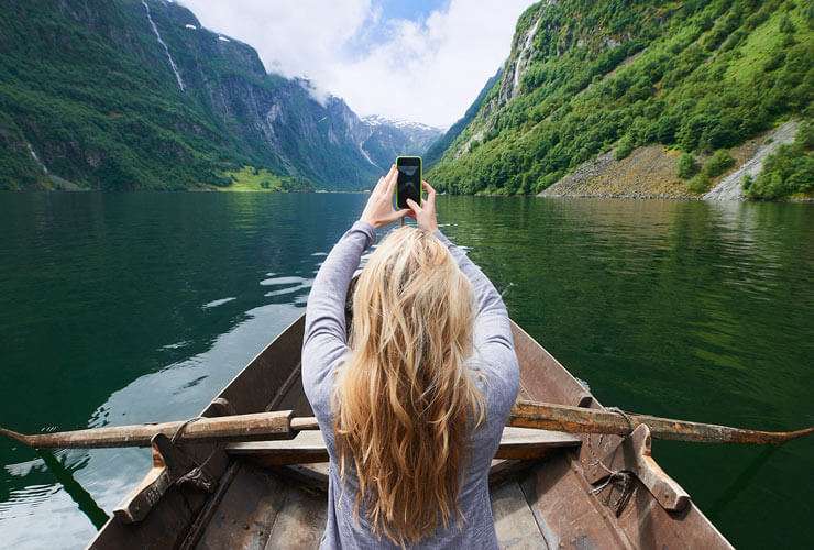 Woman in kayak films mountain scenery with mobile phone