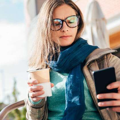 Woman outside with scarf and coffee checks her phone