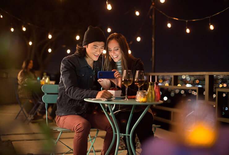 Traveling couple look at phone together in an outdoor bistro at night