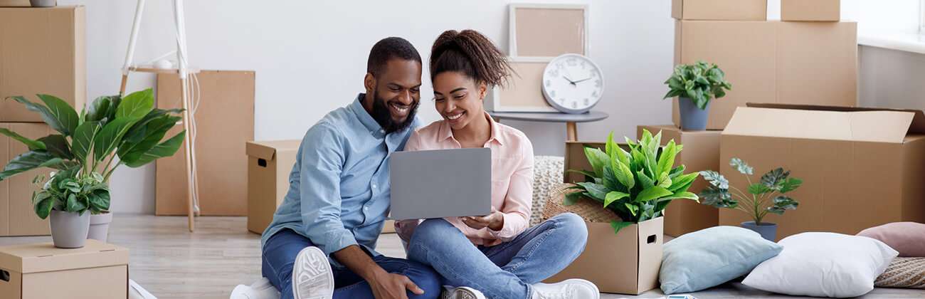 Young mixed race couple sets up internet service on their laptop while surrounded by moving boxes