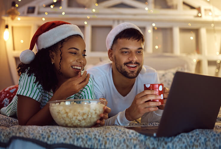 Young couple enjoys streaming movies with popcorn, holiday decorations, and Santa hats