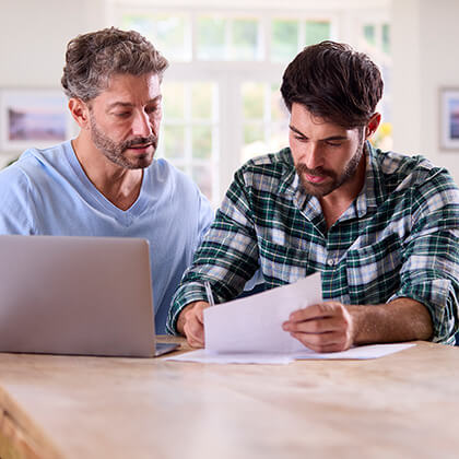 Two men looking over paper work with a laptop on table