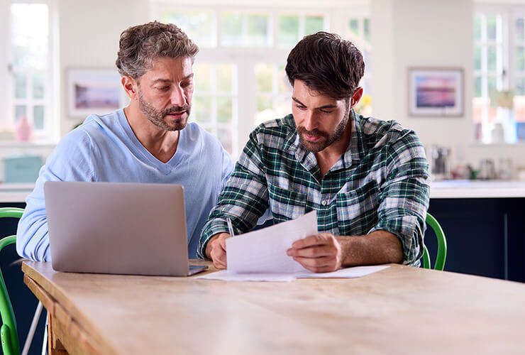 Two men looking over paper work with a laptop on table