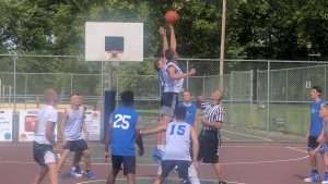 young men playing a basketball game on an outside court
