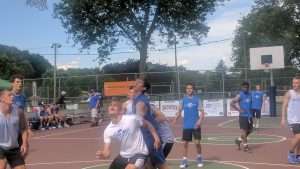 young men playing a basketball game on an outside court