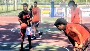 young men playing a basketball game on an outside court
