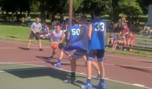 young men playing a basketball game on an outside court