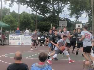 young men playing a basketball game on an outside court