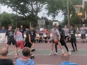 young men playing a basketball game on an outside court