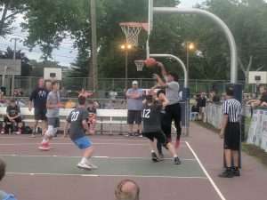 young men playing a basketball game on an outside court