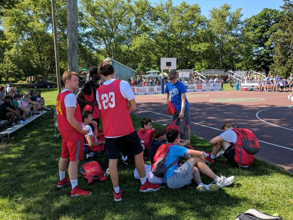 team sitting on sidelines of a high school men's outdoor basketball game