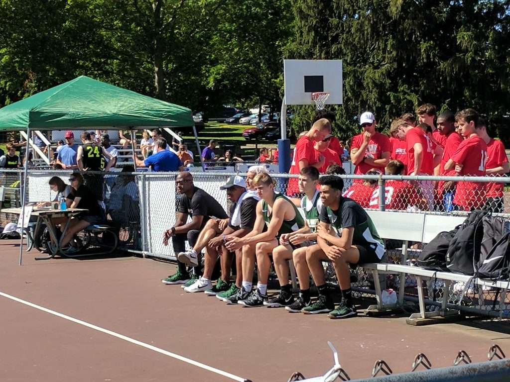 team sitting on bench at a high school men's outdoor basketball game