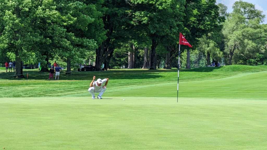 man squatting to watch golf ball on golf course