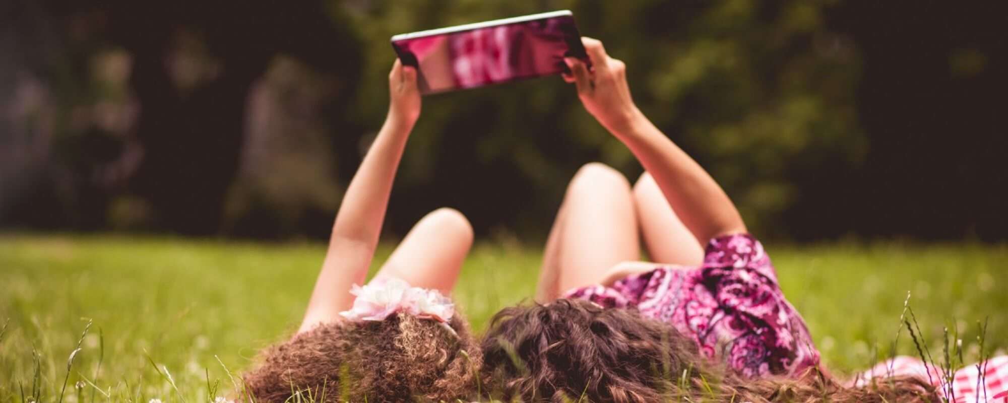 mother and daughter in a field watching a video on a tablet