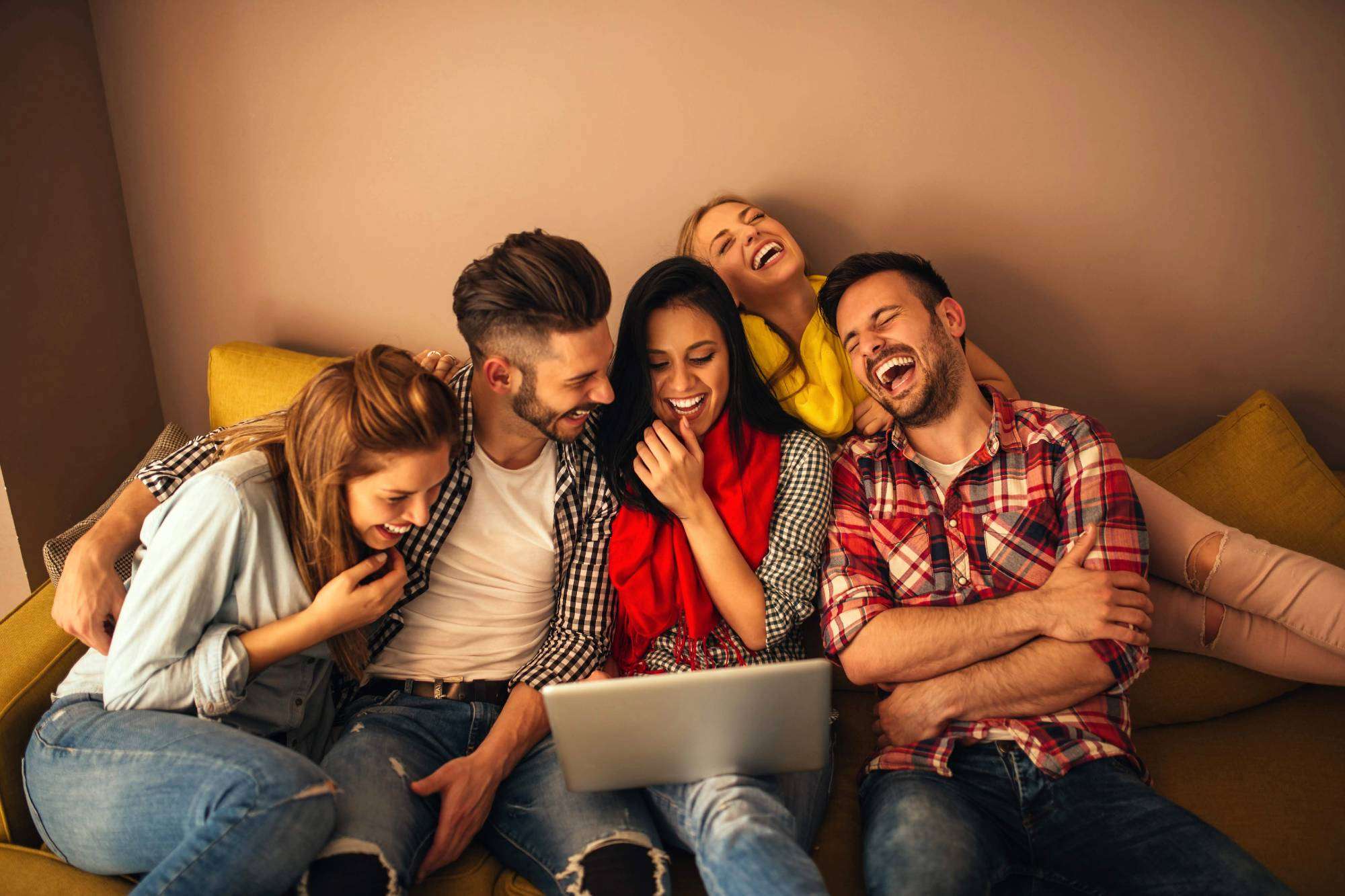 Laughing Group Of Young Adults Looking At Laptop On Couch