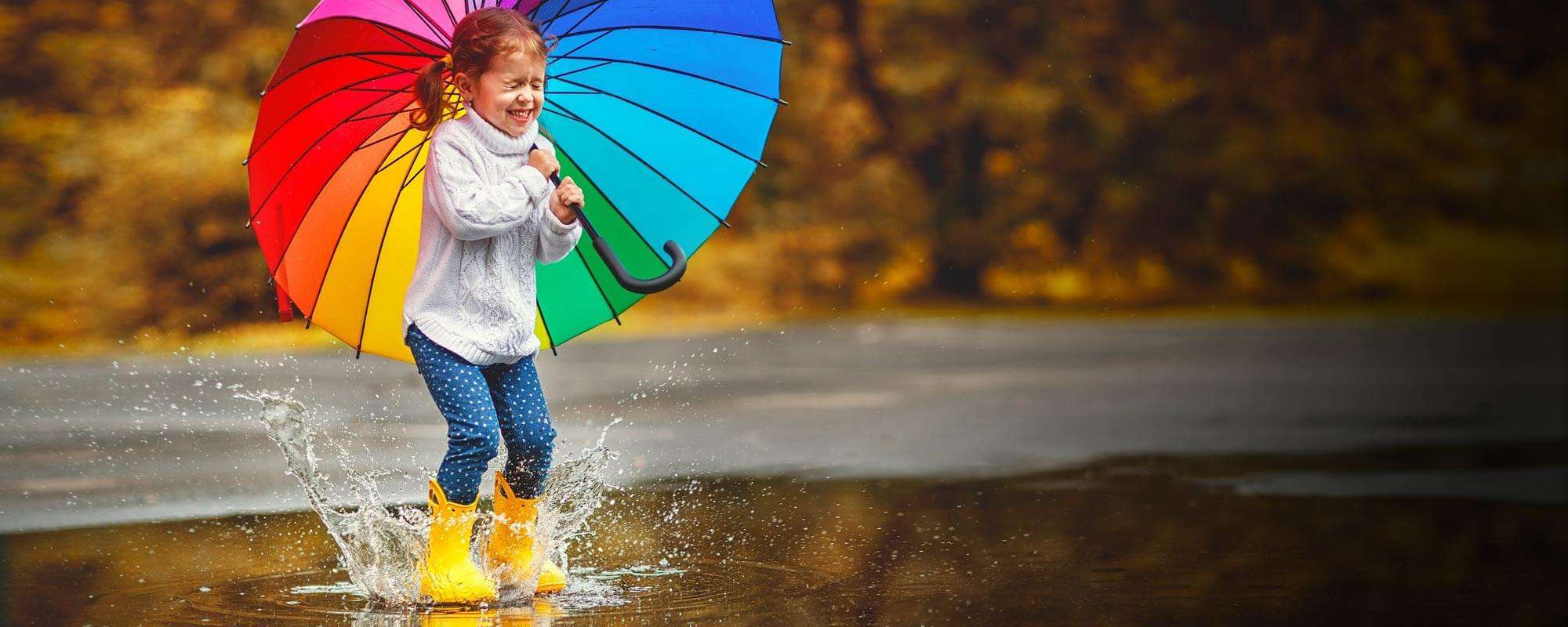 What to Watch this Spring - child with rainbow umbrella splashes in a spring rain shower