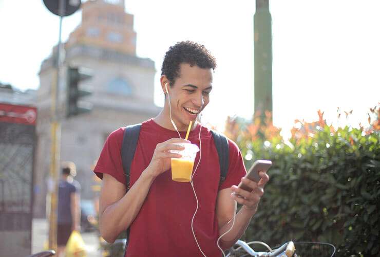 Young man outside listens to mobile phone on ear buds