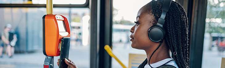Young woman in braids and headphones uses her mobile phone to board public transportation