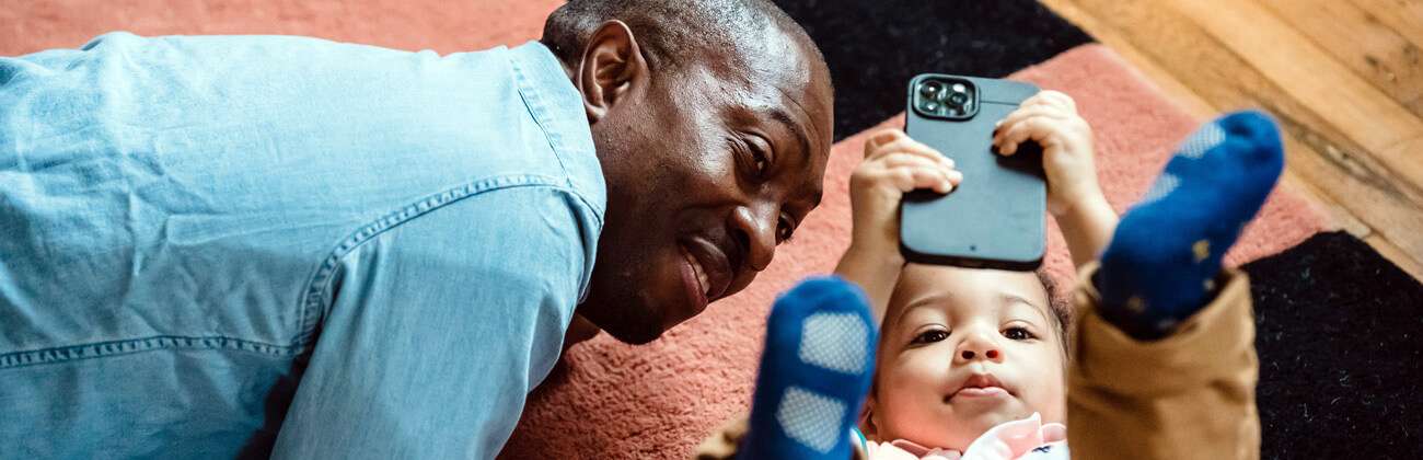 Granddad and baby lay on a rug and look at a mobile screen