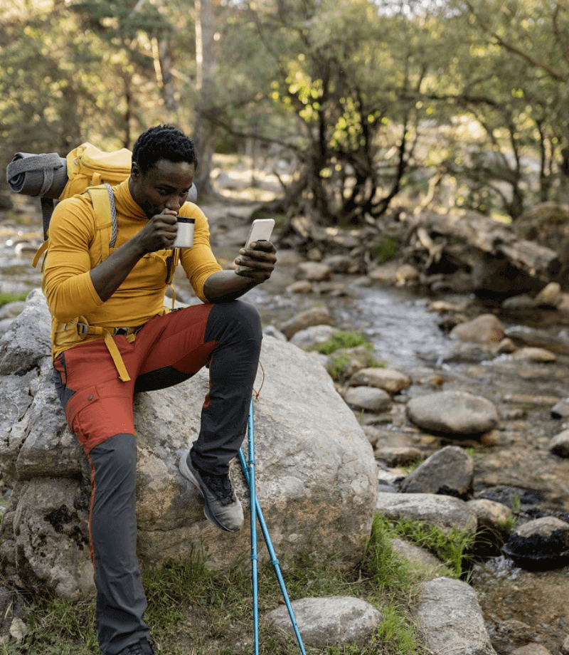Man on a hike sipping coffee and scrolling on his phone