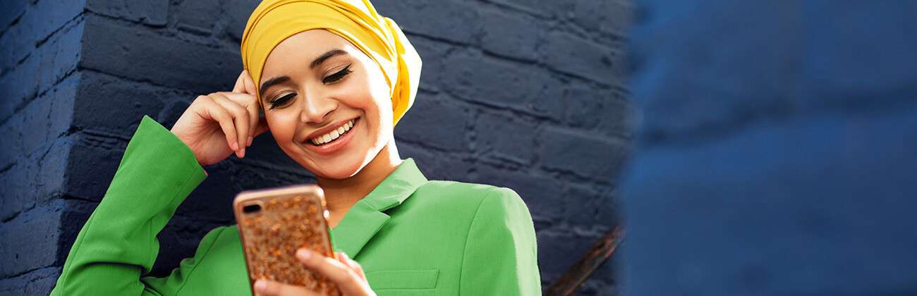 Young woman brightly dressed in hijab and jacket uses mobile device
