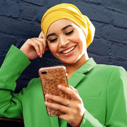 Young woman brightly dressed in hijab and jacket uses mobile device