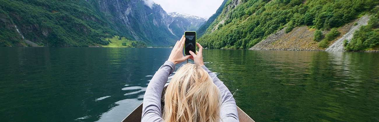 Woman in kayak films mountain scenery with mobile phone