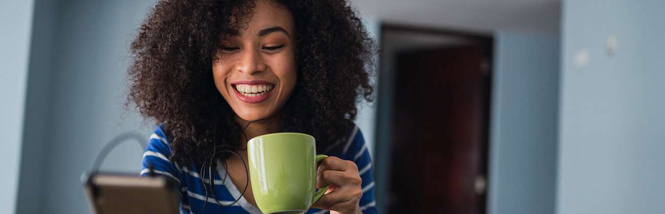 Young woman with a big 'fro and coffee mug listens to her phone with ear buds