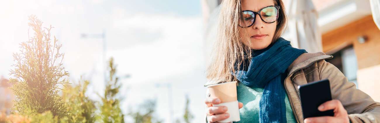 Woman outside with scarf and coffee checks her phone