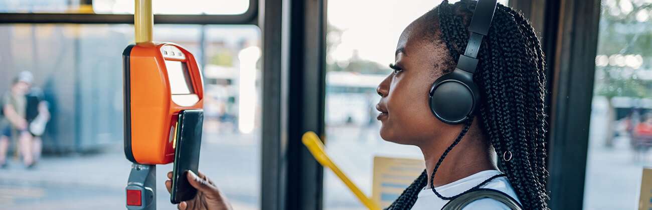 Young woman in braids and headphones uses her mobile phone to access public transportation