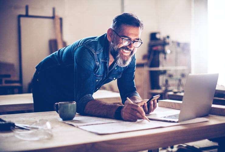 Bearded craftsman working with mobile device and laptop
