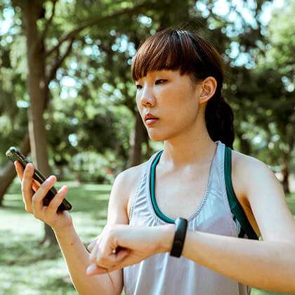Asian woman jogging in a park checks fitness monitor on her mobile device