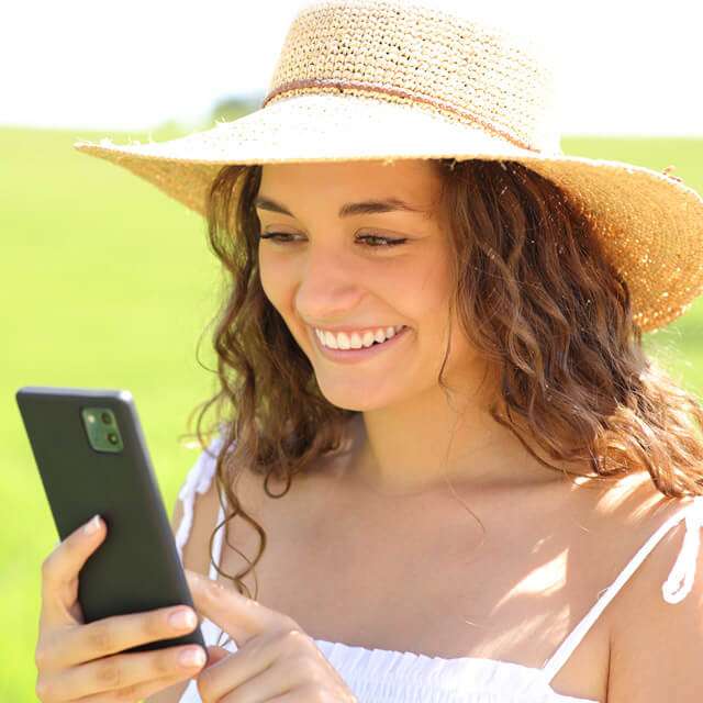 Young woman in fun summer attire and sun hat watches on her phone