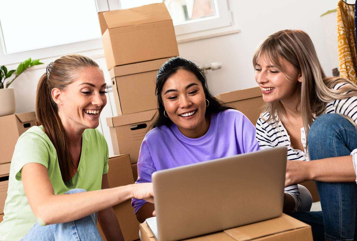 Three women set up WiFi at a new apartment using a laptop sitting on moving boxes