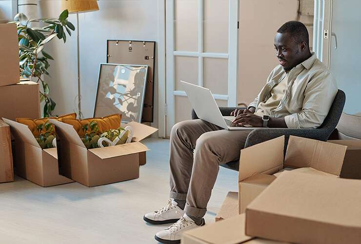 African American man on laptop surrounded by moving boxes sets up his new internet service