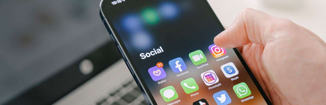 Hand selects social media icons on a mobile phone being aware of red flags that can help spot possible social media impersonation schemes such as unusual profile info, unsolicited messages, or suspicious posts.