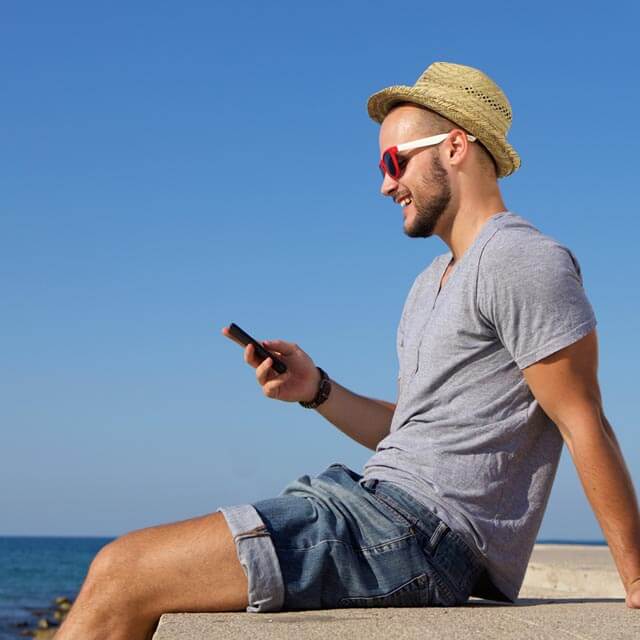 Man relaxing by the seaside uses phone to stream the latest shows
