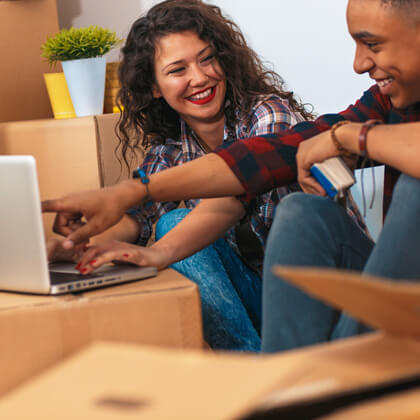 Hispanic couple surrounded by moving boxes sets up internet on their laptop.