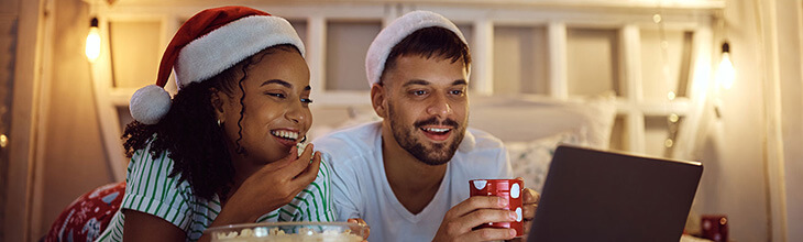 Young couple enjoys streaming movies with popcorn, holiday decorations, and Santa hats