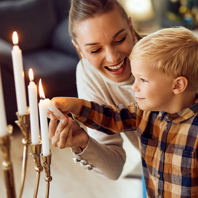 Small boy and Mom light holiday menorah for Hanukkah