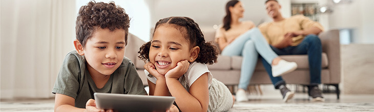 Two kids use a tablet with mom and dad in the background