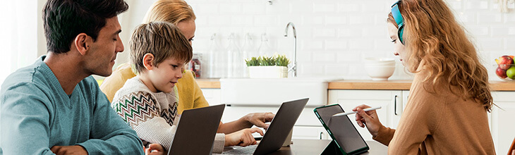 Family working around the kitchen table on multiple devices