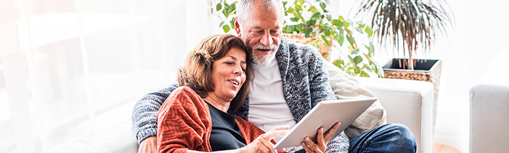 Retired couple reviews cybersecurity resources on a tablet from the comfort of their sofa