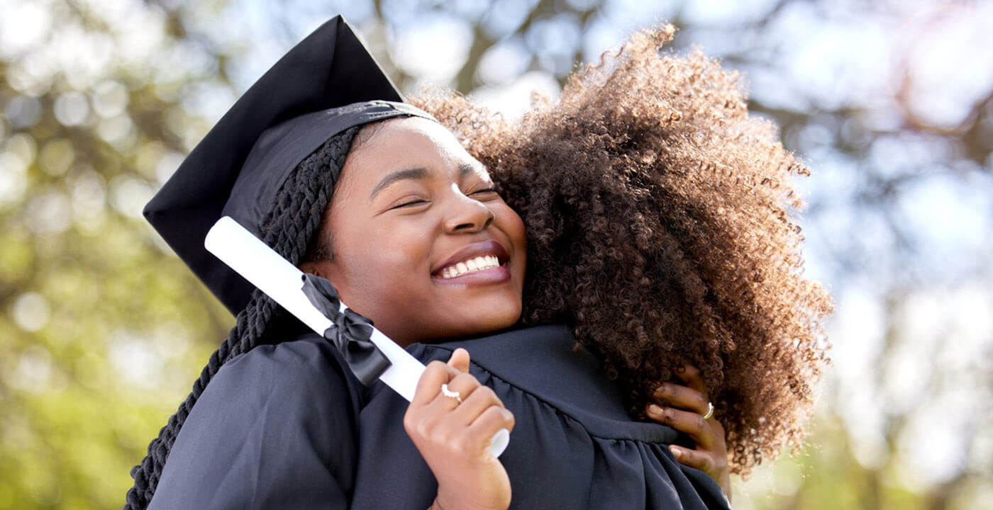 two graduates holding diplomas hug