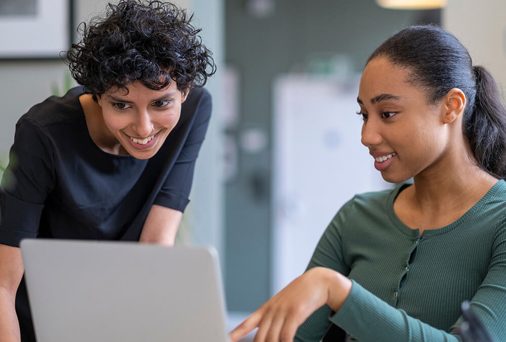 two women looking at a laptop on a desk