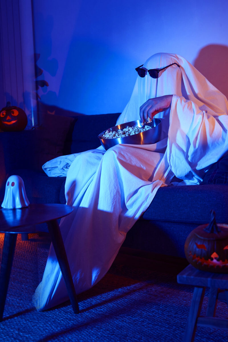 person dresses in a ghost costume watching TV and eating popcorn